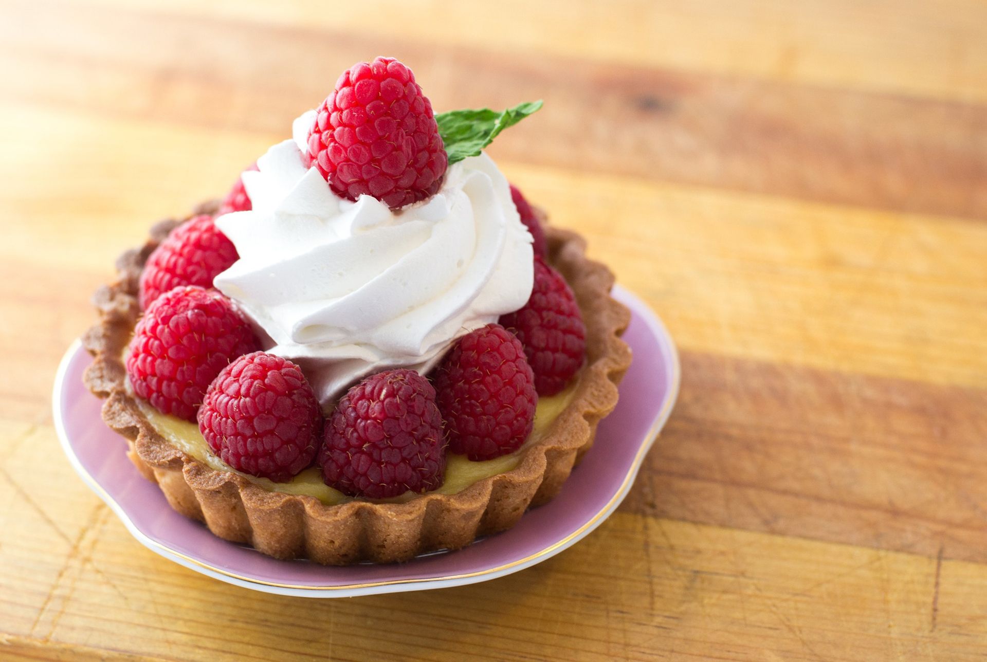 raspberry tart with whipped cream on pink plate sittonf on a wooden table